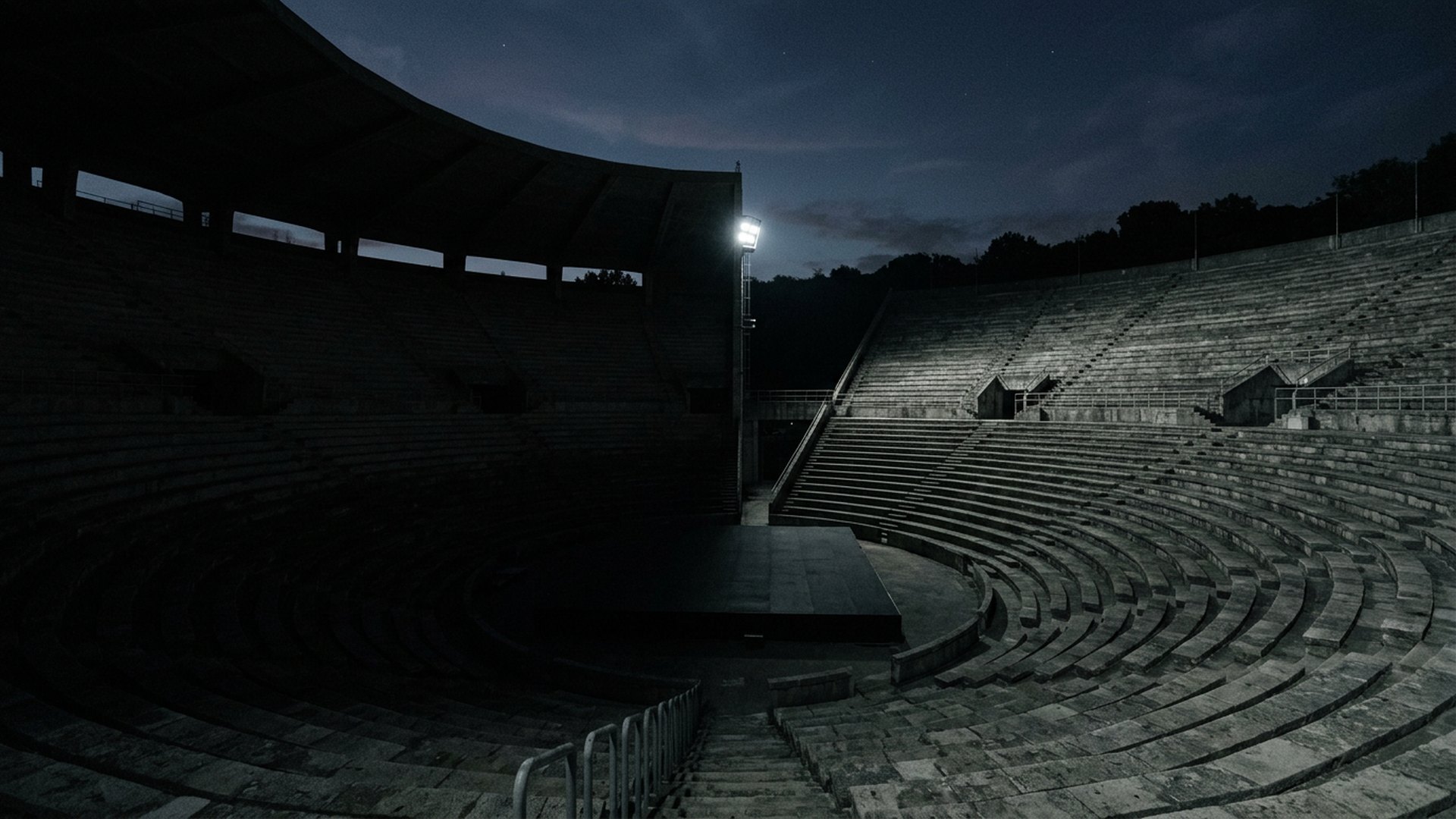 Empty concrete amphitheater at dusk under dramatic shadow and light.